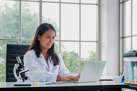 Female Doctor Sitting At Desk Working At Laptop In Officeの写真素材