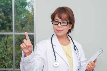 brunette female doctor standing with clipboard near window in hospital. Physician ready to examine patientの写真素材