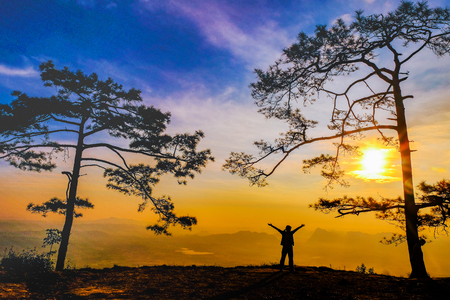 Silhouette of woman on cliff in mountains looking into sunsetの写真素材
