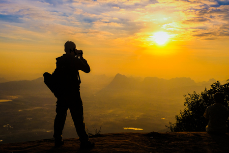 Man backpacker with her dslr camera silhouette in sunset backgroundの写真素材