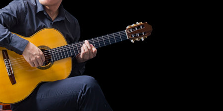 Portrait of asian man wearing playing guitar on black background looking to the guitar and copy...