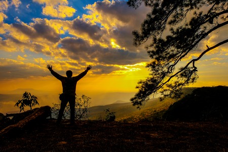 A silhouette standing on a hilltop accomplished during morning sunの写真素材