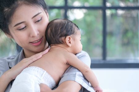 Asian mother holding a 1.5-month-old child, leaning over her shoulderの写真素材