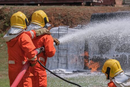 Firefighters extinguish the fire with a chemical foam coming from the fire engine through a long hose.の写真素材