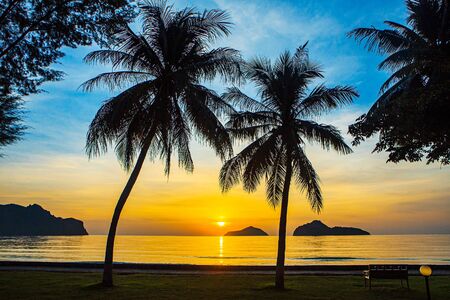 Sunrise at sea with islands and coconut trees.