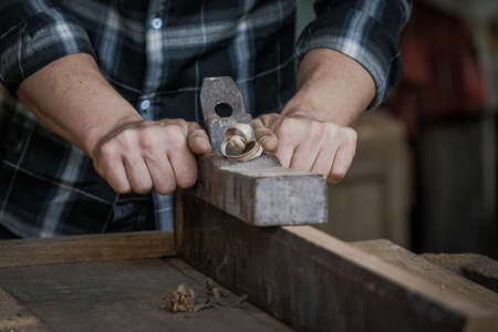 A male carpenter is using a planer to scrape the wooden surface.の写真素材