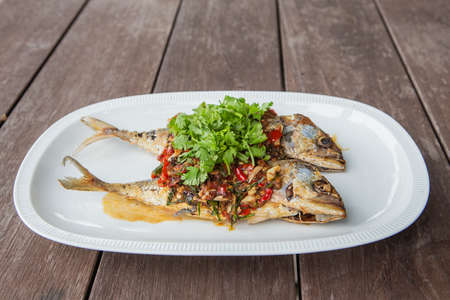 Mackerel with chili sauce in a white tiled plate on a wooden table.の写真素材