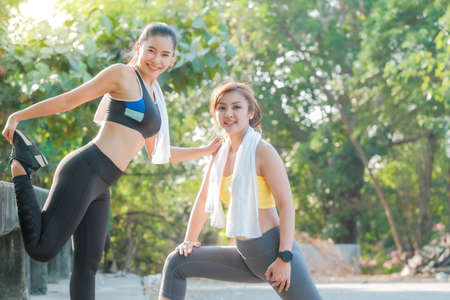 Asian women doing stretching exercises together before an evening jogging practice in the park.の写真素材