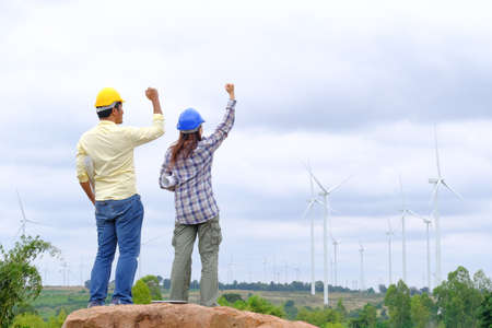 Engineers stand holding blueprints and congratulate wind turbine projects to generate electricity and check wind direction.の写真素材