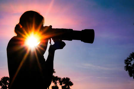 Silhouette of a woman photographer in a palm tree garden at sunriseの写真素材