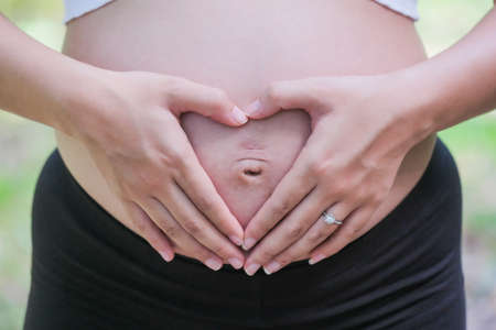 8 month pregnant woman rubs her stomach in a heart shapeの写真素材