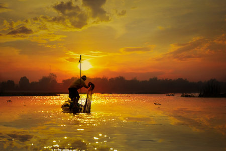 Local fishermen set sail in the morning sunlight reflecting off the sky.の写真素材
