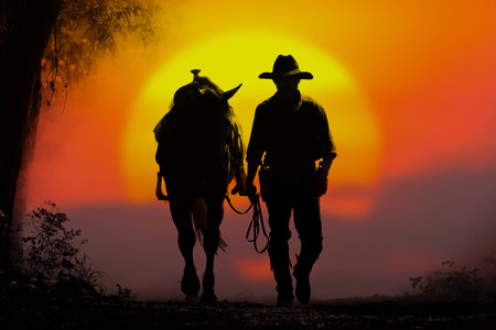 Silhouette of a cowboy leading a horse and the sunsetの写真素材