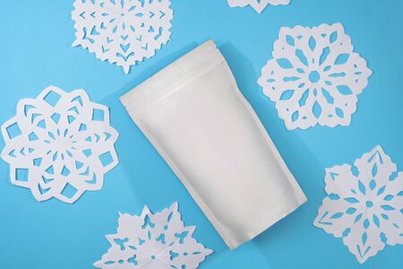 Template of paper ecological bag for storing coffee, tea on an isolated blue background with handmade snowflakes. Vacuum packaging for christmas and new year presentの写真素材