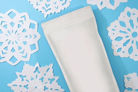 Template of paper ecological bag for storing coffee, tea on an isolated blue background with handmade snowflakes. Vacuum packaging for christmas and new year presentの写真素材