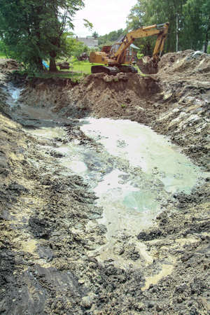 An excavator digs a large trench for building a house. A tractor digs a large lake that is already gaining water. Stock background for designの写真素材