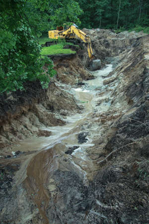 An excavator digs a large trench for building a house. A tractor digs a large lake that is already gaining water. Stock background for designの写真素材
