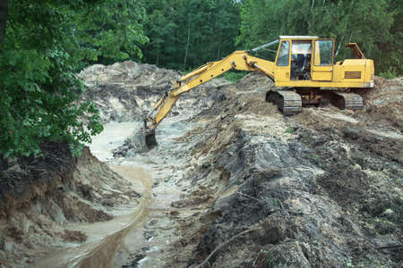 An excavator digs a large trench for building a house. A tractor digs a large lake that is already gaining water. Stock background for designの写真素材