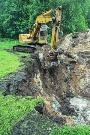 An excavator digs a large trench for building a house. A tractor digs a large lake that is already gaining water. Stock background for designの写真素材