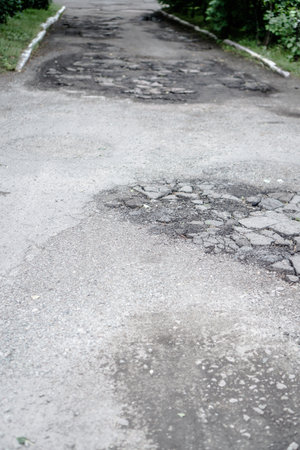 Destroyed road in poor condition requiring repair. Holes in the asphalt are filled with water and puddles. Stock photo backgroundの写真素材