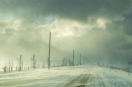 Highway with ground drifted snow illuminated by sunshine during a winter snow squall. Showing trees and power lines and poles along highway.の写真素材