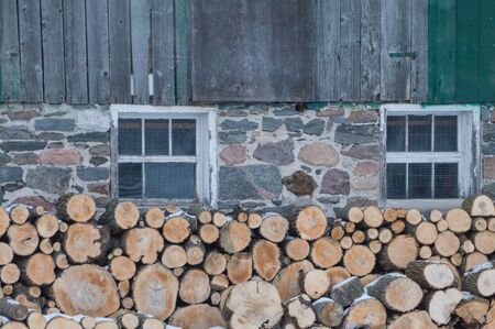 Neatly stacked firewood by an old Ontario Barn.  Barn is barnboards, field stone and has windows too. Snow on the ground.の写真素材