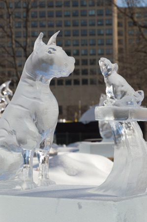 Ice sculpture in Ottawa, on a sunny day with city buildings behind.  Ice scupltrure is of two dogs, one large and one smaller one on a pedestal.のeditorial素材