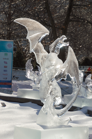 Ice sculpture in Ottawa, on a sunny day with ice covered trees behind. Ice scupltrure is of a dragon with its wings outstretched.のeditorial素材