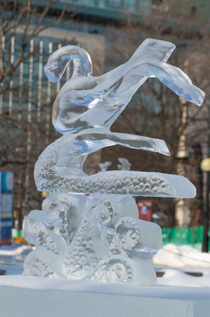 Ice sculpture in Ottawa, on a sunny day with city buildings behind.  Carving is of a large water bird, a swan or goose on waves.のeditorial素材