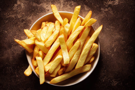 Golden French fries potatoes in bowl on brown background. Toned.の素材