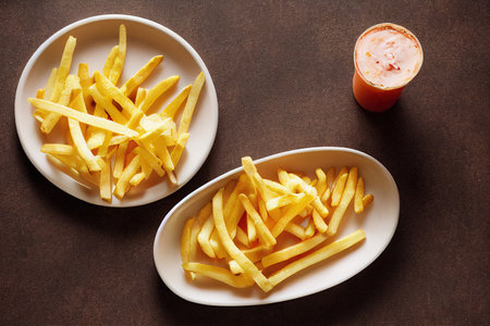 Golden French fries potatoes in white plate on dark background. Top viewの素材