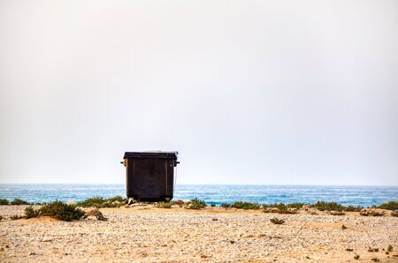 Sur, Oman. June 5, 2020. A lonely trash (garbage) can sits on the beach sand with an amazing background.の写真素材