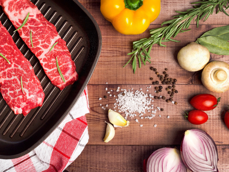 Raw meat in a frying pan on brown boards. Nearby spices, condiments and vegetables. Top of view.の写真素材