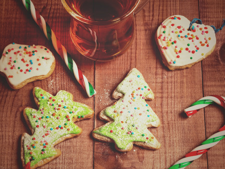 Glass mug of tea, gingerbread in the form of a Christmas tree and candy canes on a wooden background. Toned photo.の写真素材