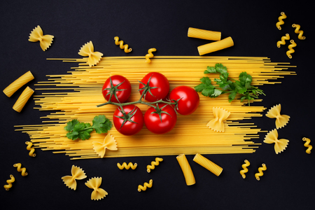 Spaghetti, greens and tomatoes on a branch on a black background.の写真素材