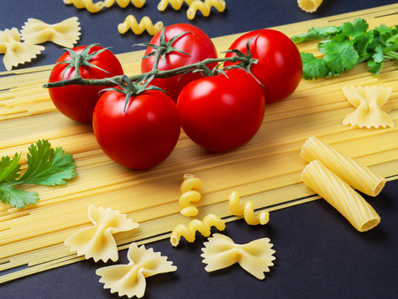 Spaghetti, greens and tomatoes on a branch on a black background.の写真素材