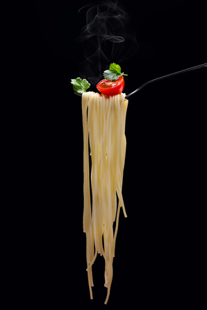Hot spagetti on the fork with tomato and parsley on the black background.Vertical.の写真素材