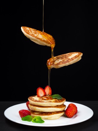Flying pancakes with honey and strawberries. Black background.の写真素材