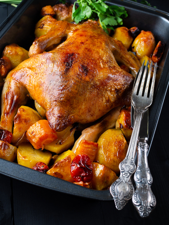 Fried chicken with vegetables on a black wooden background. Next old fork and knife. Vertical.の写真素材