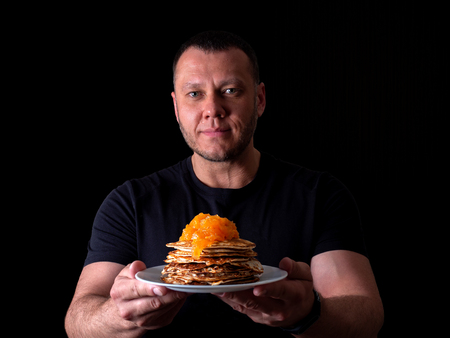 Portrait on a black background of a man with a plate of pancakes with jam.の写真素材