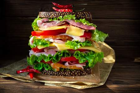 A tall sandwich on brown wooden boards. Rustic photo.の写真素材