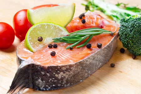 Salmon steak with lime, spices and vegetables on a wooden background.の写真素材