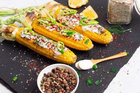 Grilled corn with cream sauce, spices, jalapeno on the black stone tileの写真素材