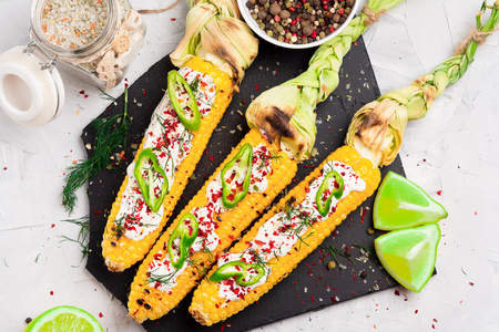Grilled corn with cream sauce, spices, jalapeno on the black stone tileの写真素材