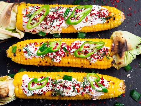 Grilled corn with cream sauce, spices, jalapeno on the black stone tile.の写真素材
