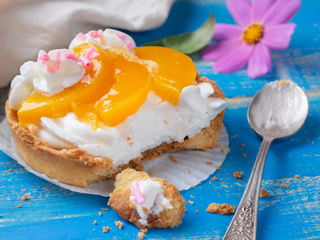 Tartlets with curd cream and peaches on a blue wooden background, spoon and flower nearの写真素材