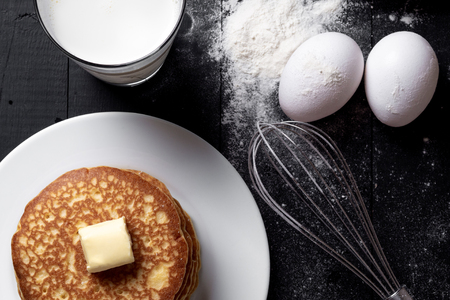 Ingredients for pancakes: milk, eggs, flour, butter on a black background. Top of view.の写真素材