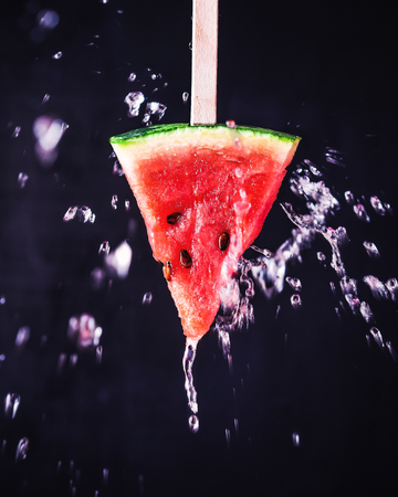 Slice of watermelon on a stick with a spray on a dark backgroundの写真素材