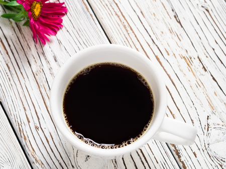 A cup of coffee and a red flower on an old wooden tableの写真素材