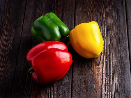 green, yellow and red bell peppers on dark brown wooden background. Well suited for the catalog.の写真素材